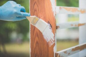 Expert painter applying paint to a residential wood fence to improve durability and appearance in New Hampshire - Paint or Stain Your Fence?